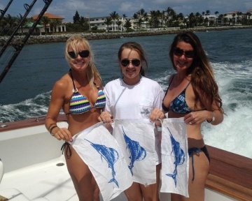 three women holding blue marlin flags on a boat